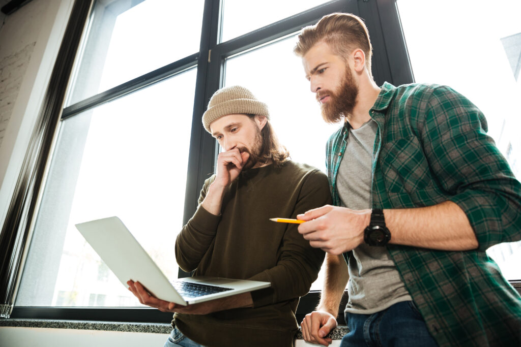 Young concentrated men colleagues in office using laptop